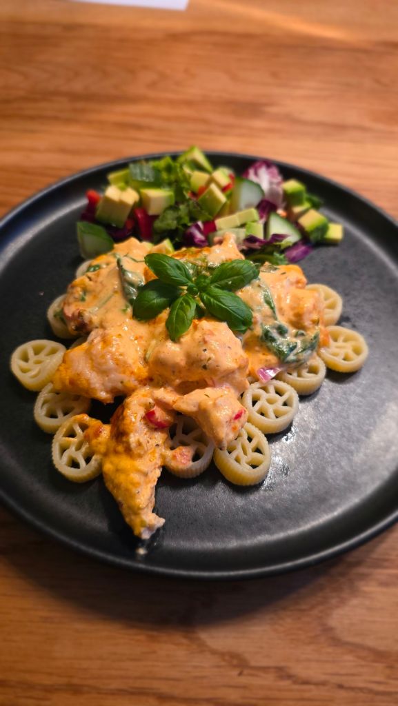 Krämig kyckling i paprikapestosås serverad med hjulformad pasta och avokadosallad.